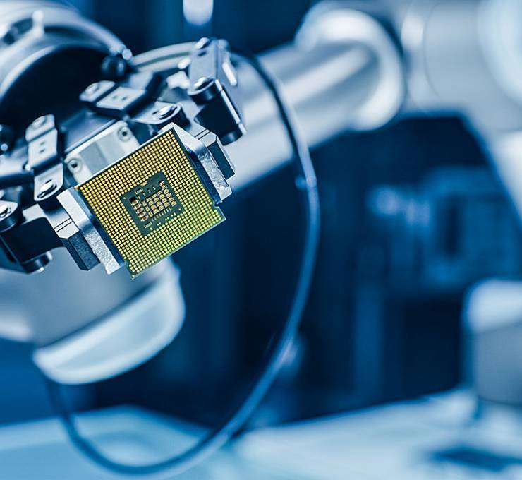 Robotic arm holding computer processor chip with golden pins, blue high-tech background blurred, precision gripping mechanism visible.
